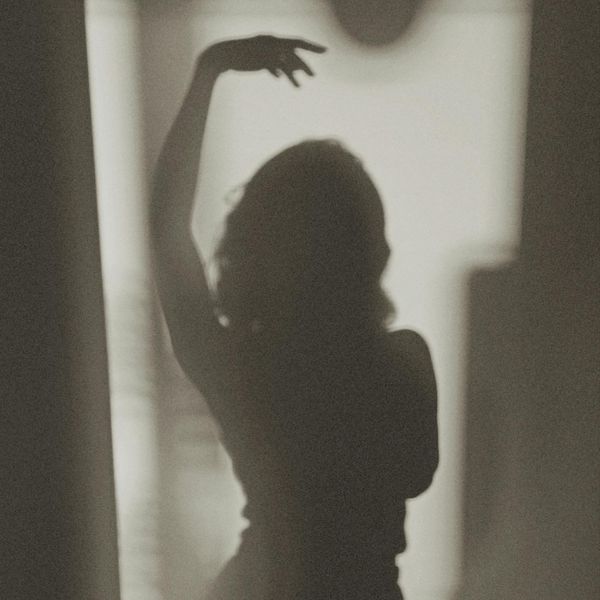Silhouette of a woman in a graceful stretching pose against a soft background.